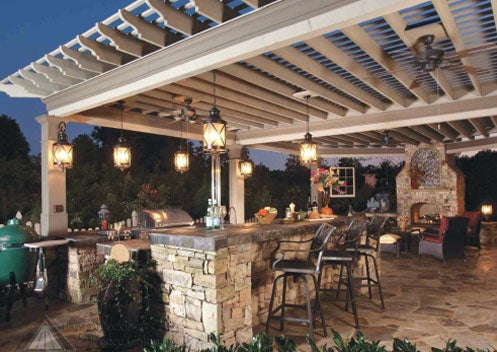 Outdoor patio with stone bar, pergola, lighting, and cozy seating area.