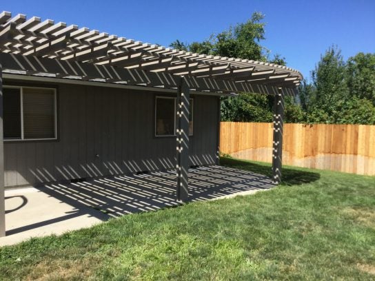 Wooden attached pergola casting beautiful shadows over a backyard patio