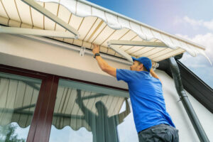 Professional installing a window awning for home protection outdoors.